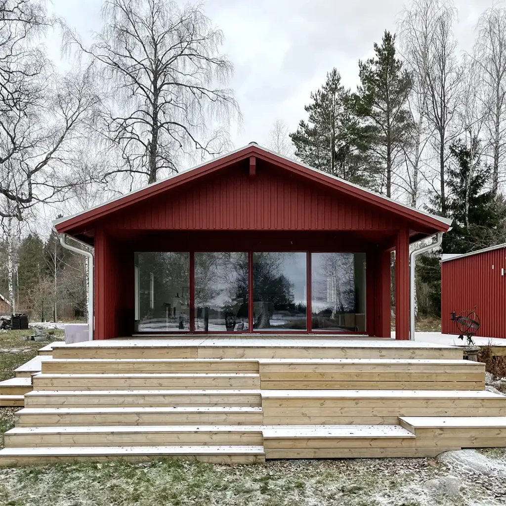 Renoverat fritidshus vid sjö med ljus faluröd träfasad och zinkdetaljer
